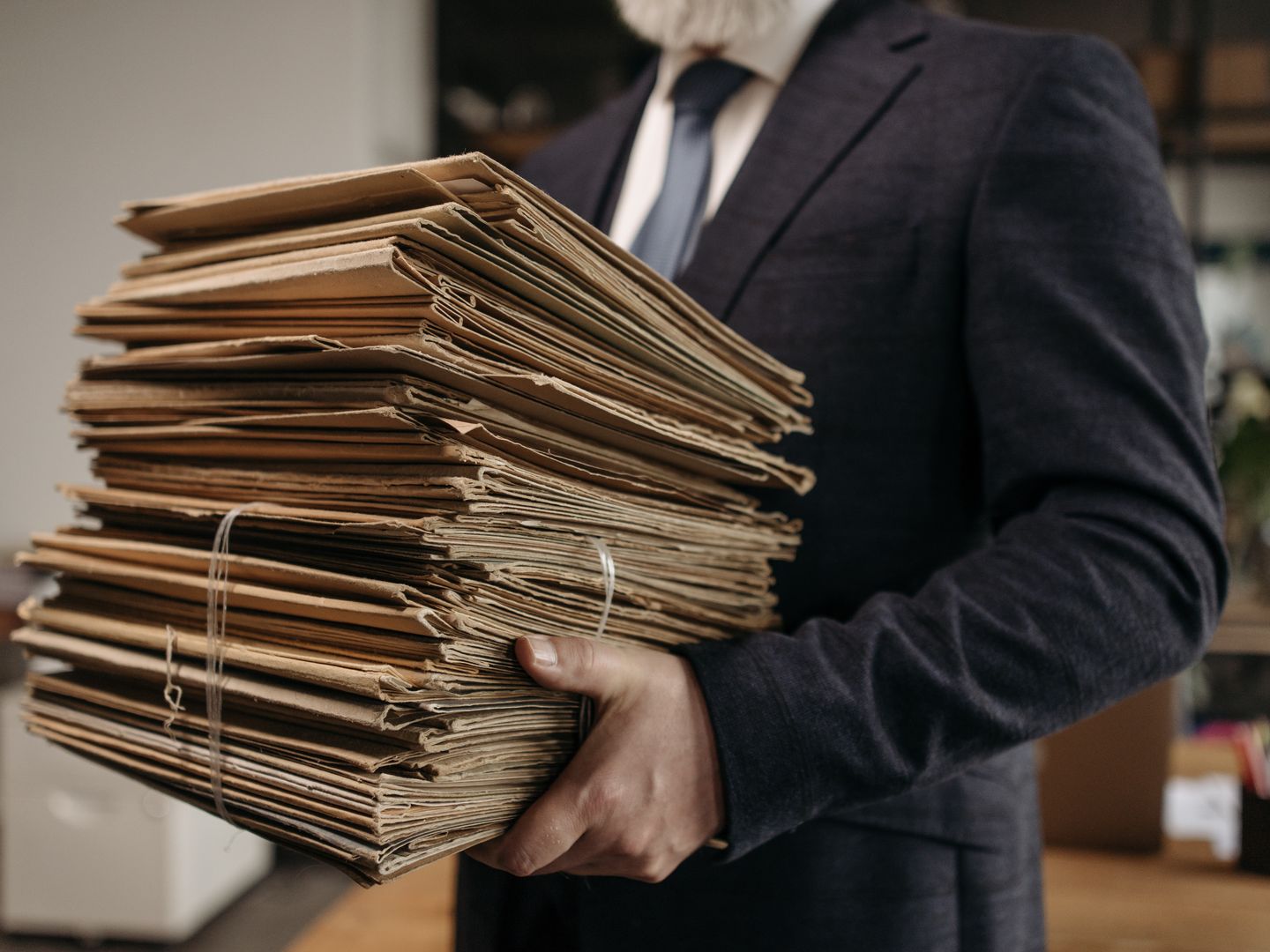 Close up of business professional holding a large stack of brown folders in an office setting.