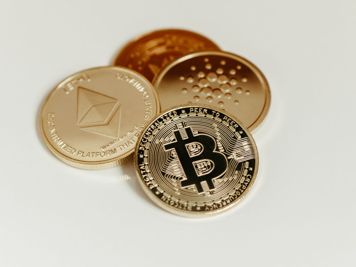 Close up of Bitcoin, Ethereum, and Cardano coins on a plain background, showcasing digital currency.